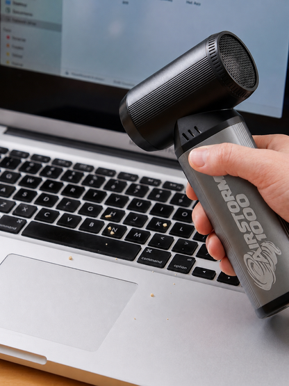 A hand using the AirStorm 1000 to clear crumbs from a laptop keyboard