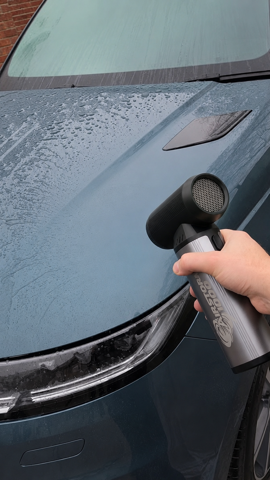 A hand using the AirStorm 1000 to blow water droplets off the hood of a freshly washed car