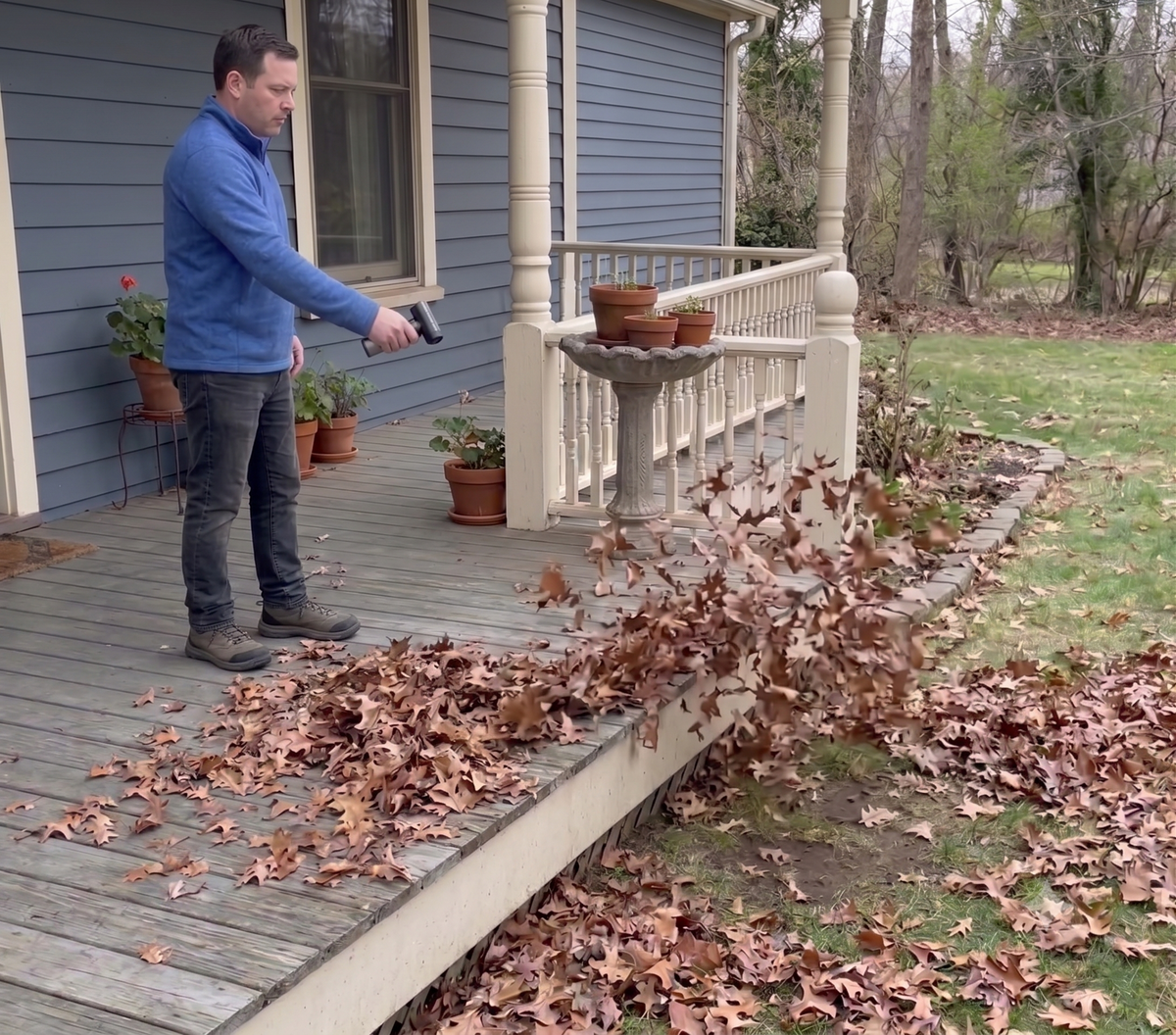 A person using the AirStorm 1000 to clear fallen leaves off a wooden porch deck
