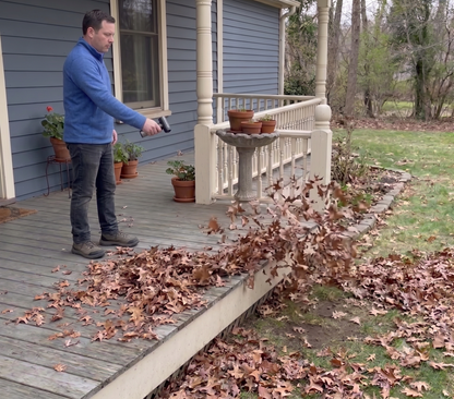 A person using the AirStorm 1000 to clear fallen leaves off a wooden porch deck